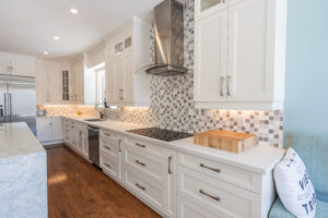 Bright transitional kitchen with custom white shaker cabinets, oversized quartz island, glass display cabinets, mosaic backsplash, and stainless steel appliances.