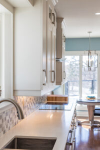 Bright transitional kitchen with custom white shaker cabinets, oversized quartz island, glass display cabinets, mosaic backsplash, and stainless steel appliances.