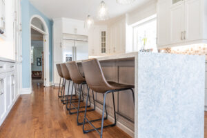 Bright transitional kitchen with custom white shaker cabinets, oversized quartz island, glass display cabinets, mosaic backsplash, and stainless steel appliances.