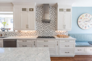 Bright transitional kitchen with custom white shaker cabinets, oversized quartz island, glass display cabinets, mosaic backsplash, and stainless steel appliances.