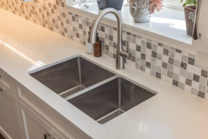 Bright transitional kitchen with custom white shaker cabinets, oversized quartz island, glass display cabinets, mosaic backsplash, and stainless steel appliances.