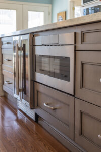 Bright transitional kitchen with custom white shaker cabinets, oversized quartz island, glass display cabinets, mosaic backsplash, and stainless steel appliances.