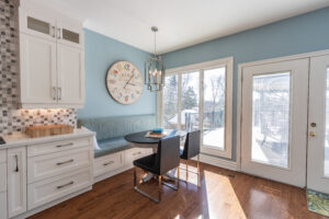 Bright transitional kitchen with custom white shaker cabinets, oversized quartz island, glass display cabinets, mosaic backsplash, and stainless steel appliances.