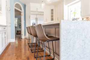 Bright transitional kitchen with custom white shaker cabinets, oversized quartz island, glass display cabinets, mosaic backsplash, and stainless steel appliances.
