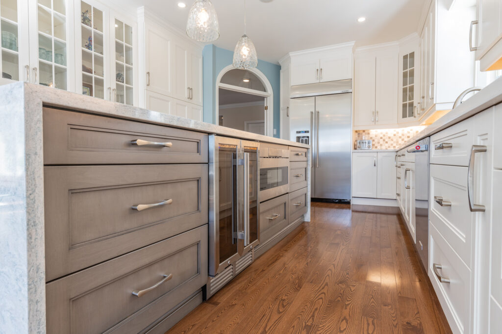 Bright transitional kitchen with custom white shaker cabinets, oversized quartz island, glass display cabinets, mosaic backsplash, and stainless steel appliances.