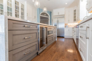 Bright transitional kitchen with custom white shaker cabinets, oversized quartz island, glass display cabinets, mosaic backsplash, and stainless steel appliances.