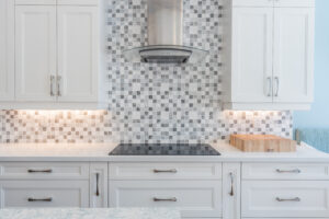Bright transitional kitchen with custom white shaker cabinets, oversized quartz island, glass display cabinets, mosaic backsplash, and stainless steel appliances.