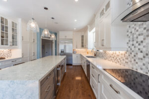 Bright transitional kitchen with custom white shaker cabinets, oversized quartz island, glass display cabinets, mosaic backsplash, and stainless steel appliances.