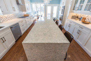 Bright transitional kitchen with custom white shaker cabinets, oversized quartz island, glass display cabinets, mosaic backsplash, and stainless steel appliances.