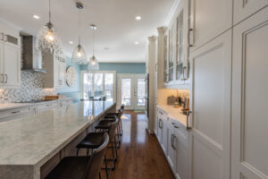 Bright transitional kitchen with custom white shaker cabinets, oversized quartz island, glass display cabinets, mosaic backsplash, and stainless steel appliances.