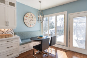 Bright transitional kitchen with custom white shaker cabinets, oversized quartz island, glass display cabinets, mosaic backsplash, and stainless steel appliances.